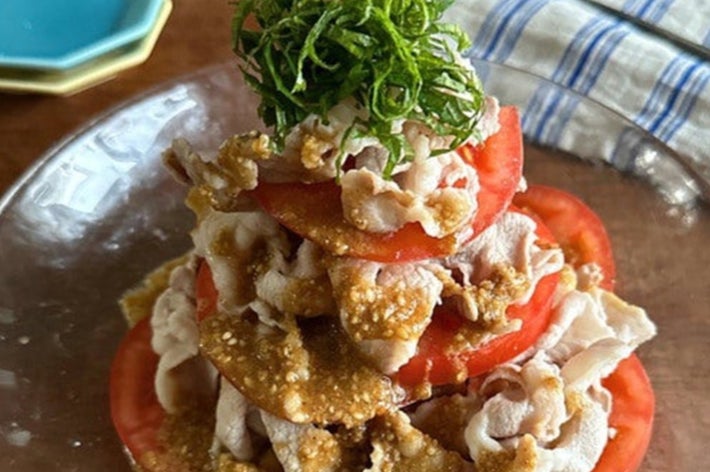 トマトと薄切り豚肉のサラダ、ゴマ風味のドレッシングがかかり、上に刻み青じそがのっている。