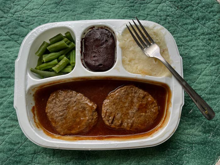 TV dinner with salisbury steaks, gravy, mashed potatoes, green beans, and a dessert, served in a sectioned plastic tray with a fork