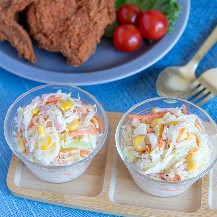 フライドチキンとトマトが後ろにあるコールスロー2つがテーブルに置かれた食事シーン。