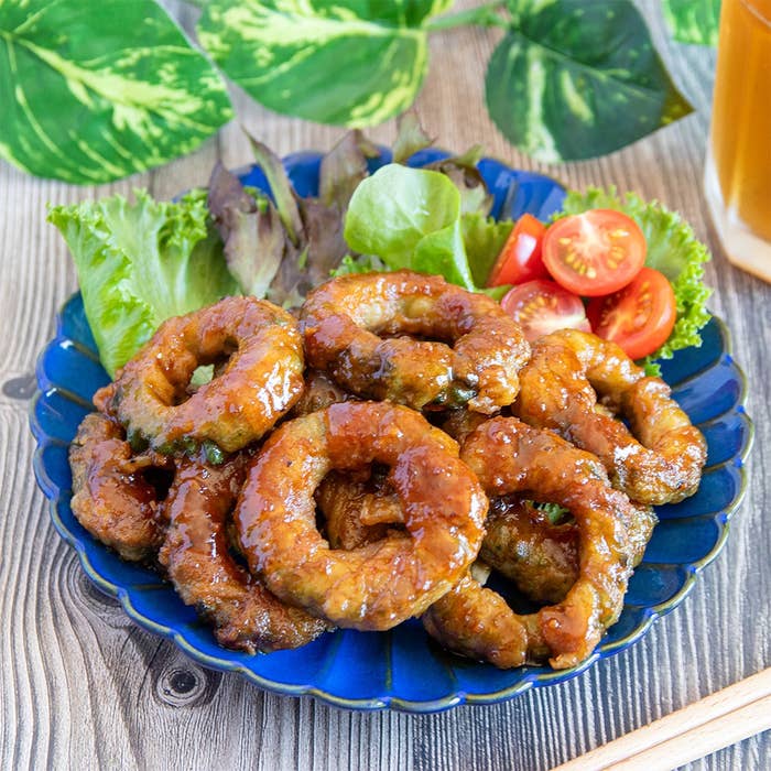 青い皿に盛られたゴーヤの肉巻き。葉物野菜とプチトマトが添えられている。