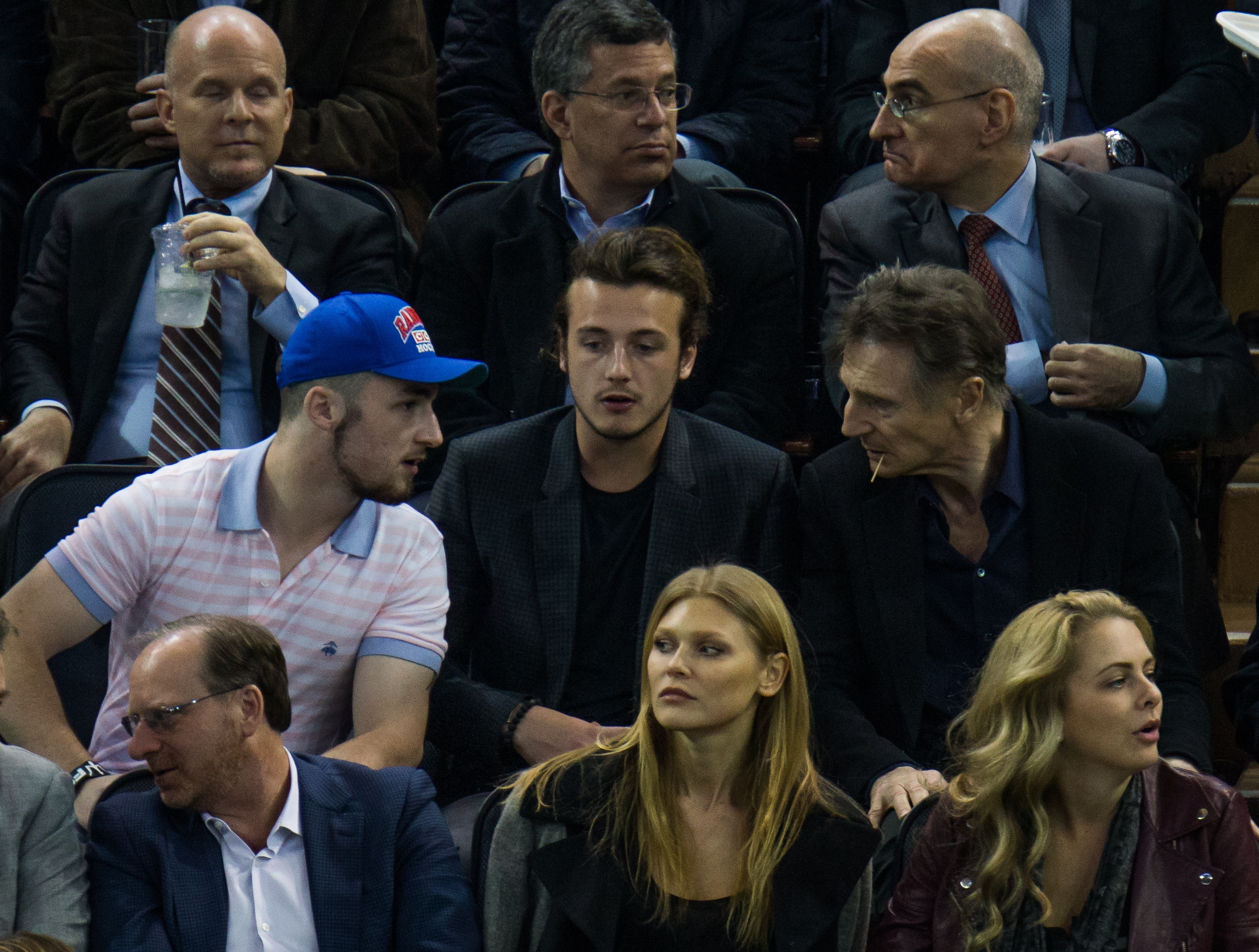 People seated in a stadium, casually dressed. The focus is on a group of seven individuals talking among themselves