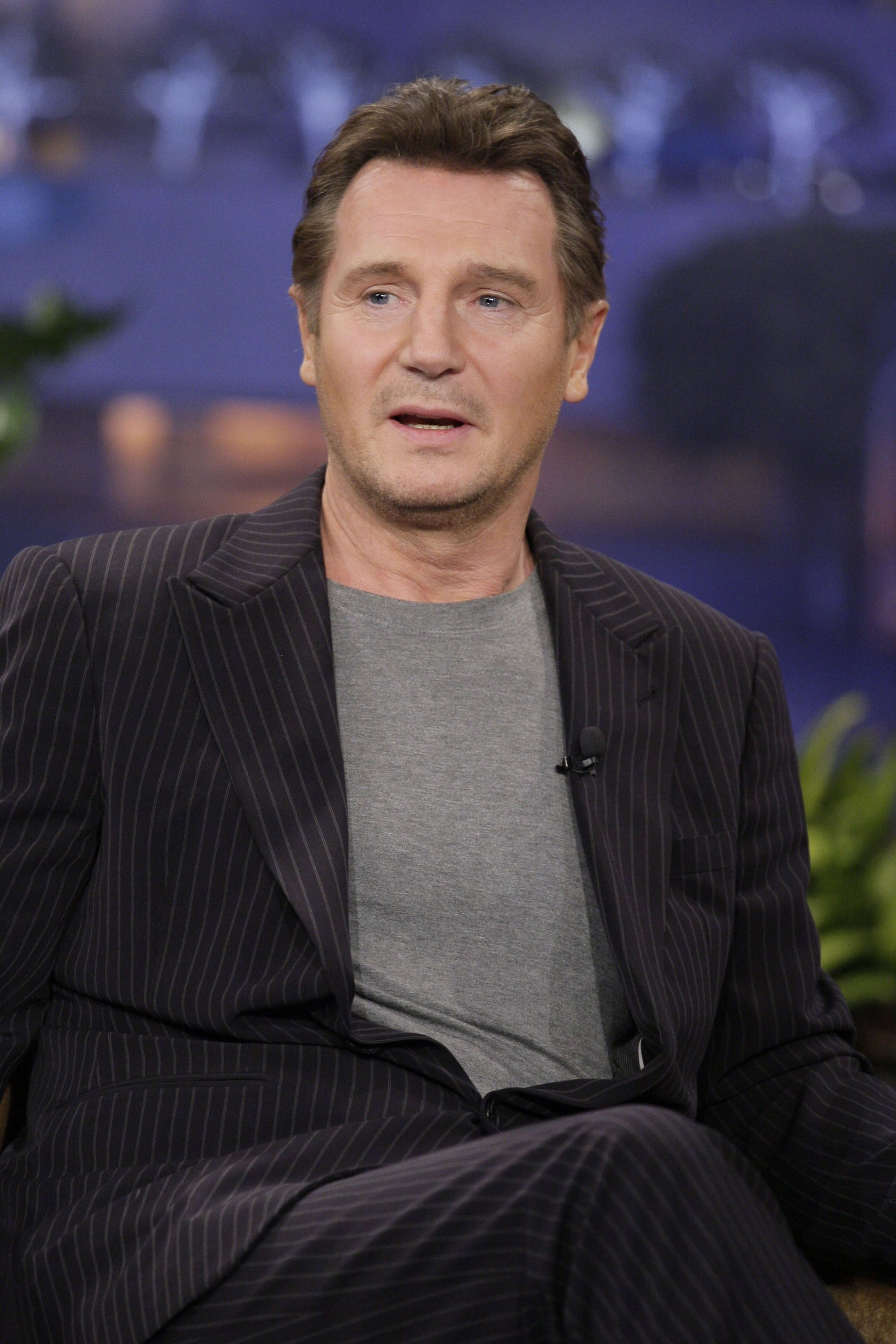 Person in pinstripe suit and gray shirt sitting on a talk show set