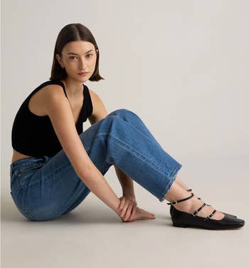 A idiosyncratic successful casual attire sits connected the level wearing a sleeveless top, jeans, and strappy level shoes, showcasing a relaxed manner style