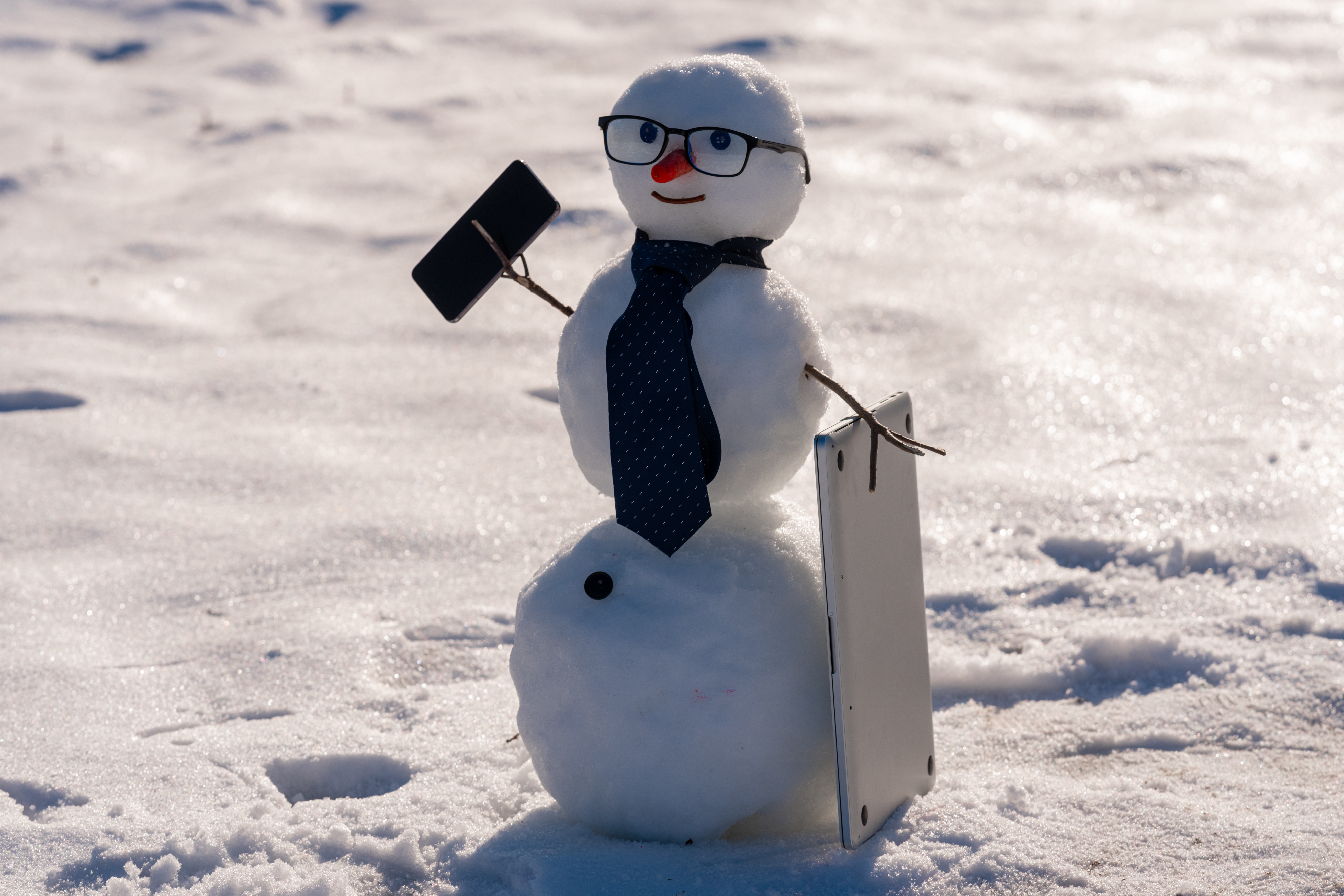 Snowman with glasses, tie, holding a smartphone and a tablet, stands on a snowy surface