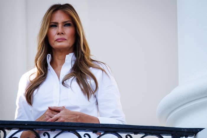 Person stands on a balcony wearing a white button-up shirt, looking ahead with a serious expression