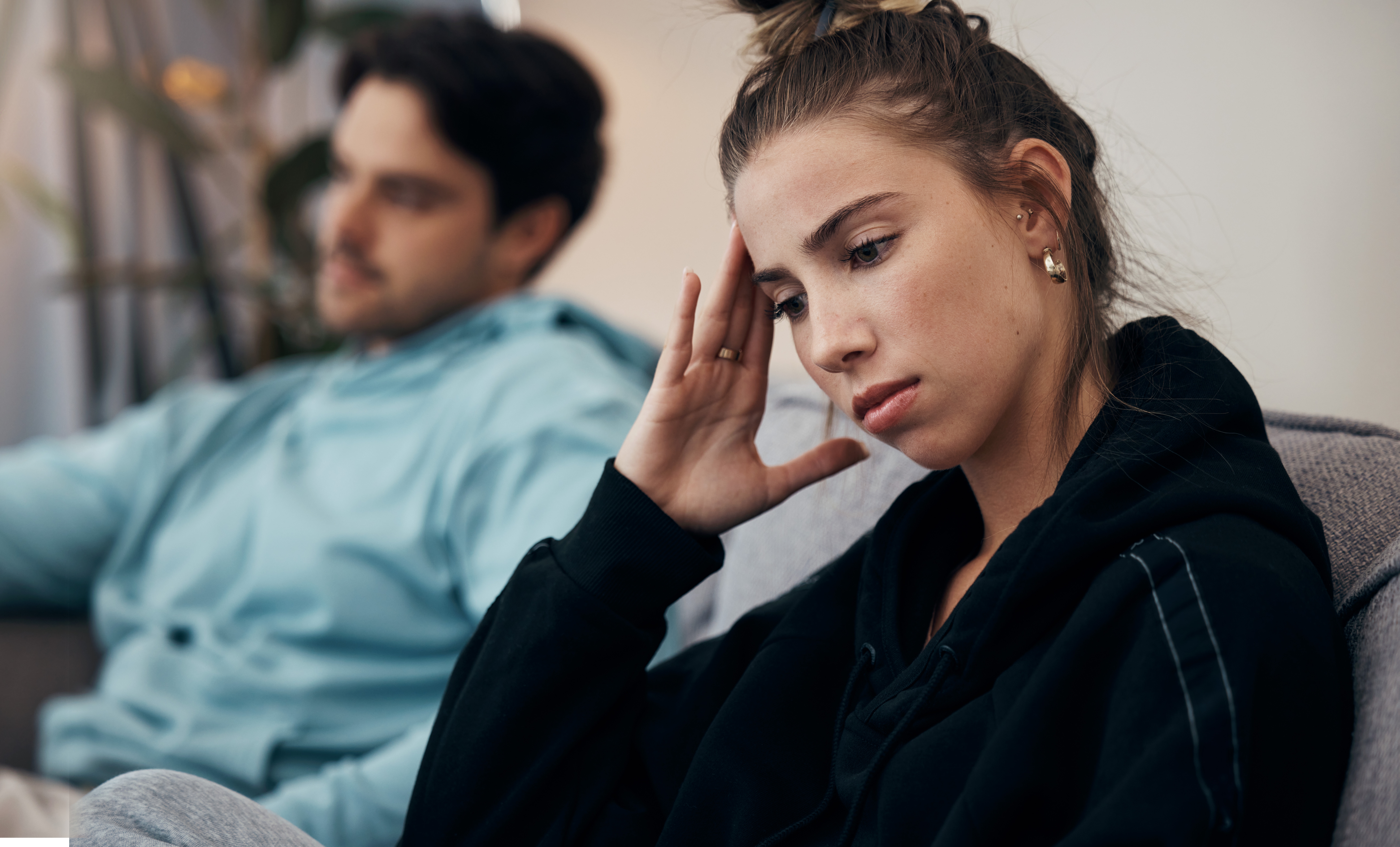 Woman in casual clothing looking thoughtful, sitting beside a relaxed person. Both appear deep in thought, possibly discussing a relationship