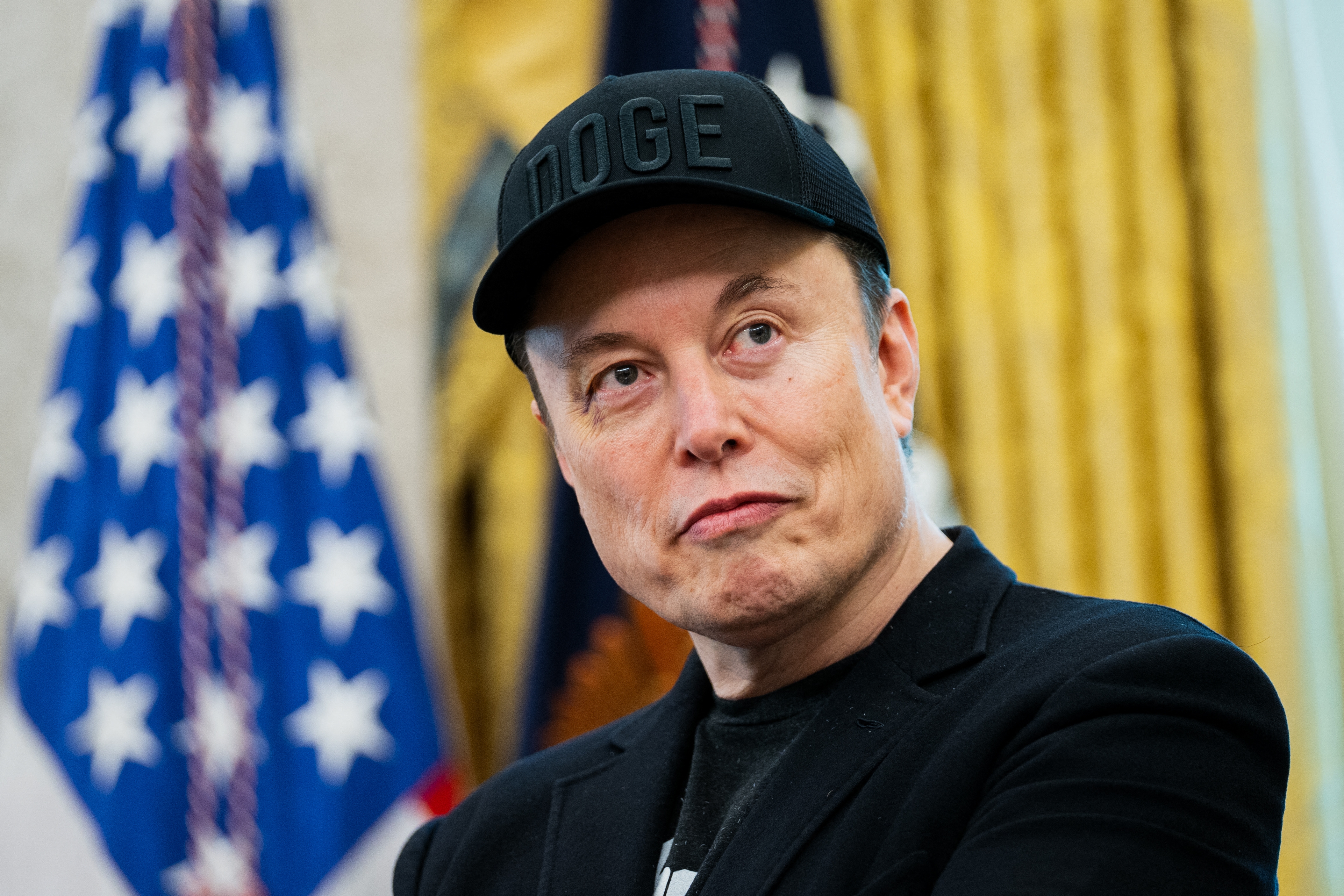 I don&#x27;t know who this is. The person wears a cap and a black jacket, standing in front of a flag in an official setting