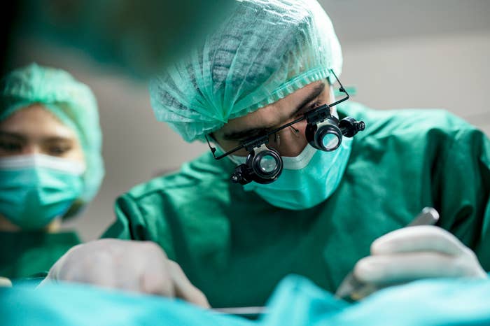 Surgeon wearing magnifying glasses and a surgical mask focuses intently while performing an operation in an operating room