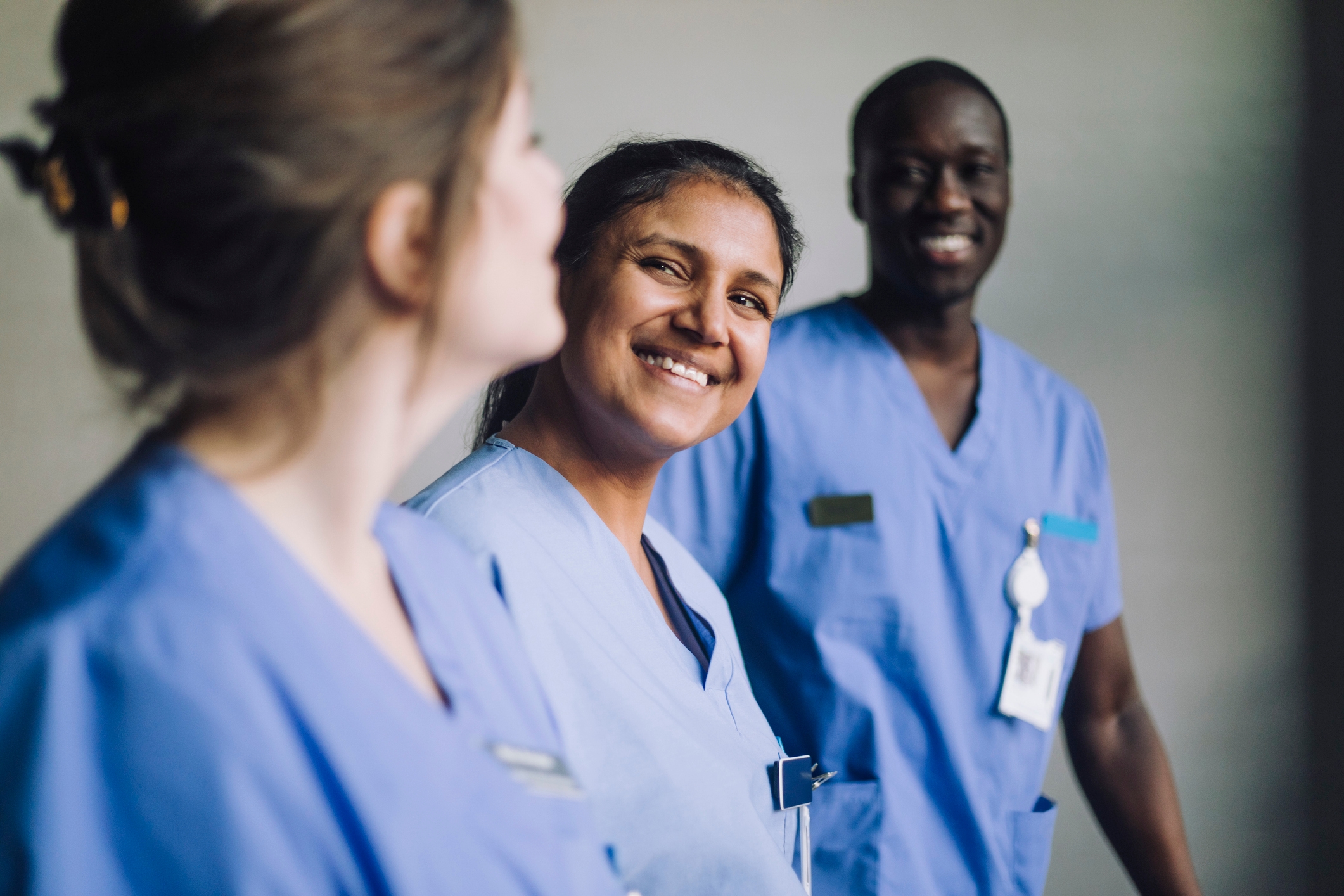 Three healthcare workers in scrubs, smiling and standing together