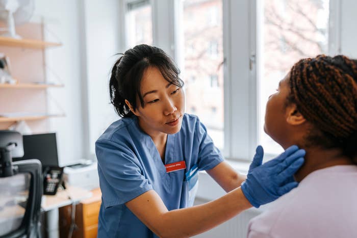 A healthcare professional in scrubs examines a patient's neck in a medical office setting