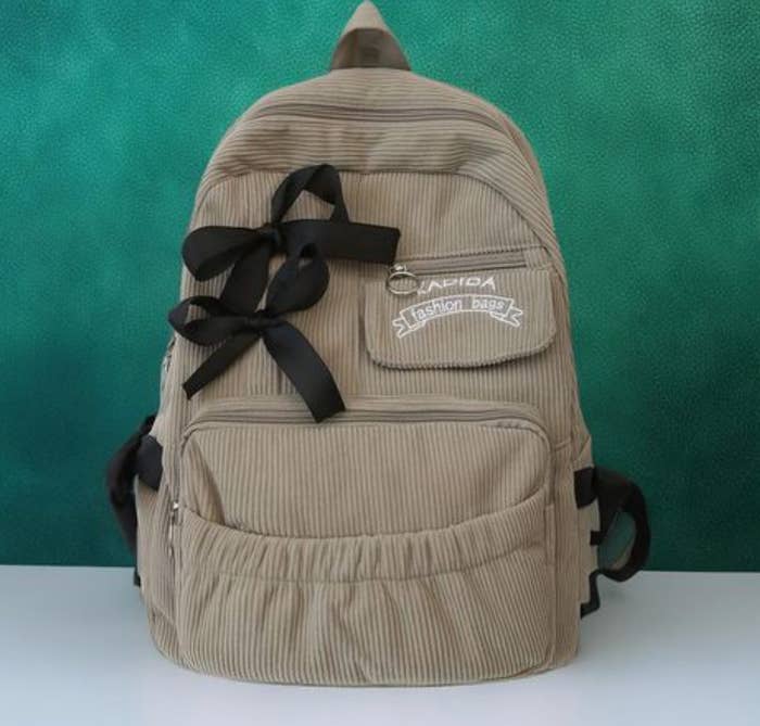 Mochila de terciopelo con cinta negra, varios compartimentos y cremalleras, sobre una superficie blanca