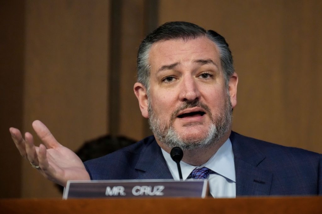A man with a beard is speaking from behind a podium, gesturing with his hand in an expressive manner
