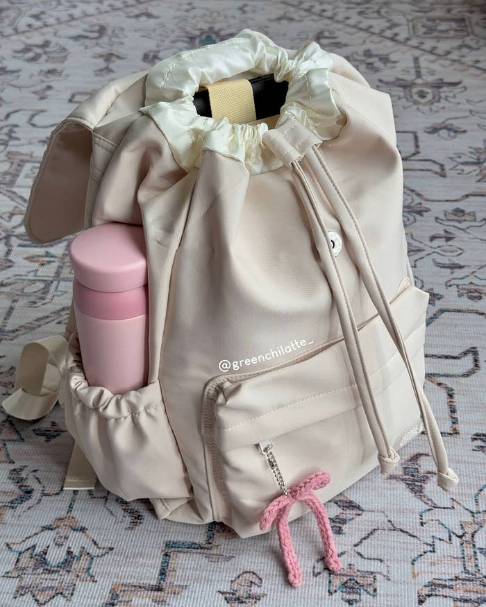 Mochila con cordón, bolsillo delantero con un llavero de cuerda rosa y una botella rosa en un bolsillo lateral
