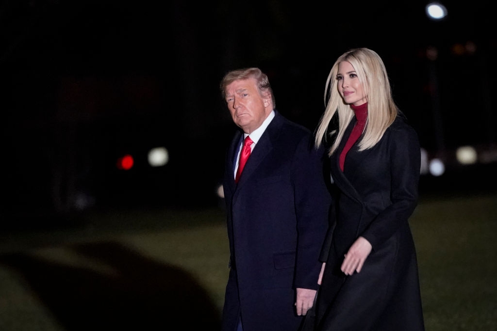 Two people walking outdoors at night. One wears a dark overcoat, the other a black coat over a red turtleneck, both with serious expressions
