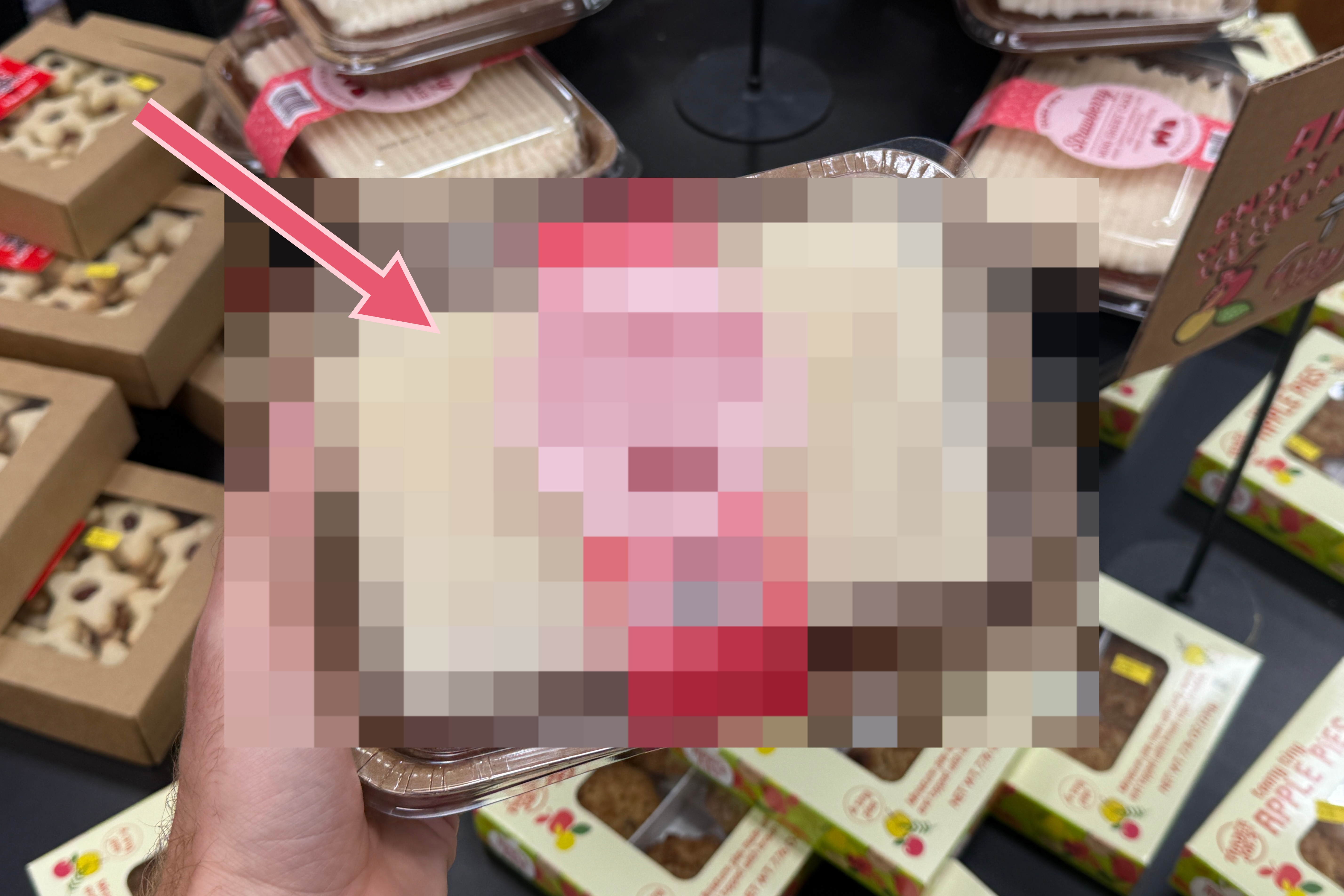 A person holding a packaged food container in a store aisle with various baked goods and snacks displayed