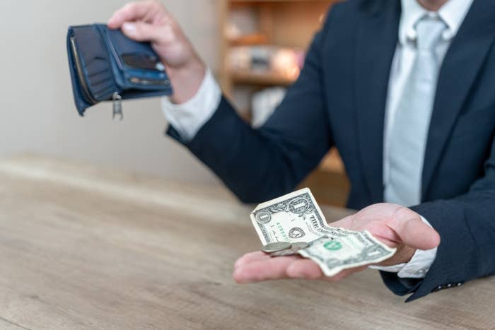 Person in a suit holding an open wallet and displaying cash and coins on a table