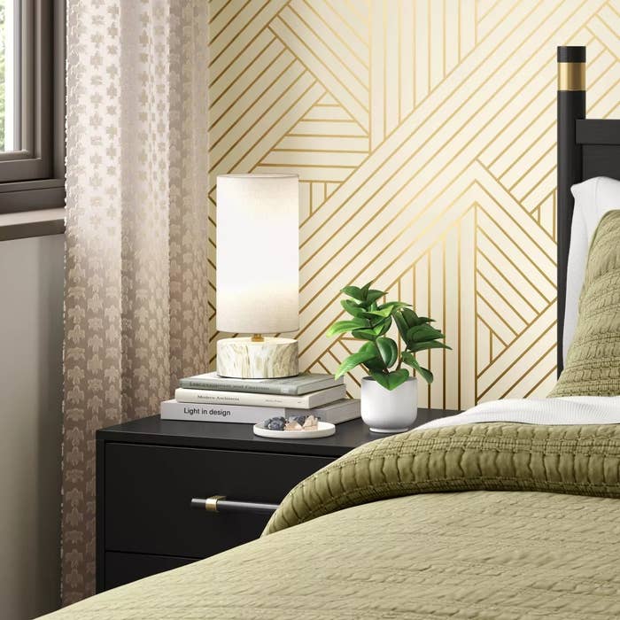 Modern chamber with geometric wallpaper, bedside array with lamp, plant, and books. Neutral-toned bedding creates a cozy and stylish atmosphere