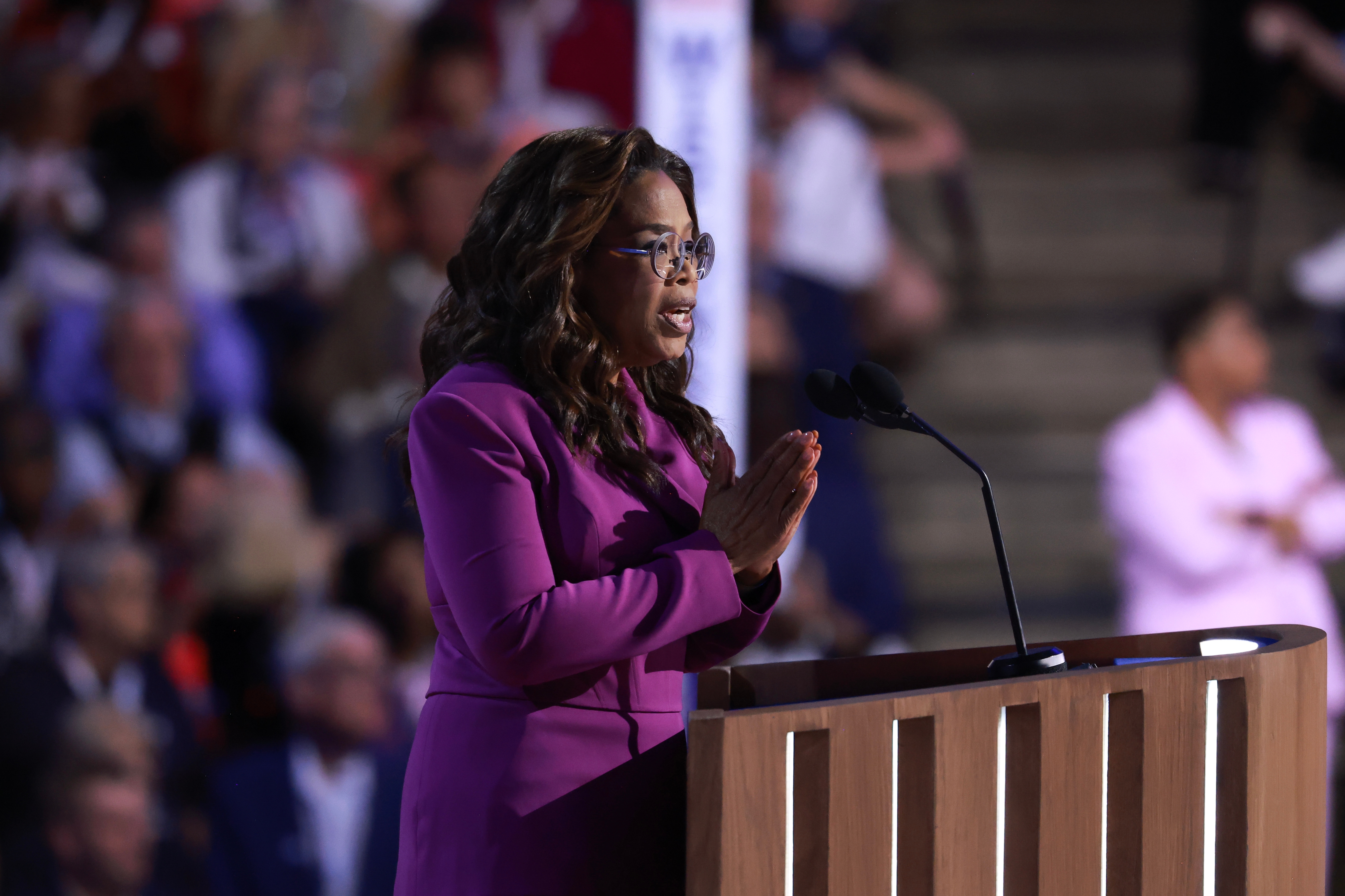 Oprah in elegant attire speaks passionately at a podium, gesturing with her hands
