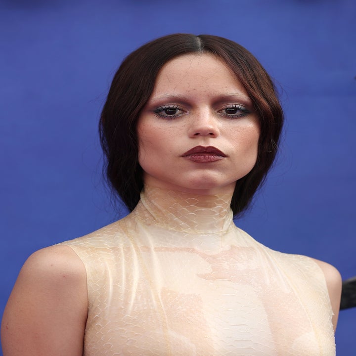 A person with long dark hair poses in a textured, semi-sheer high-neck top, styled in a sophisticated and minimalistic manner