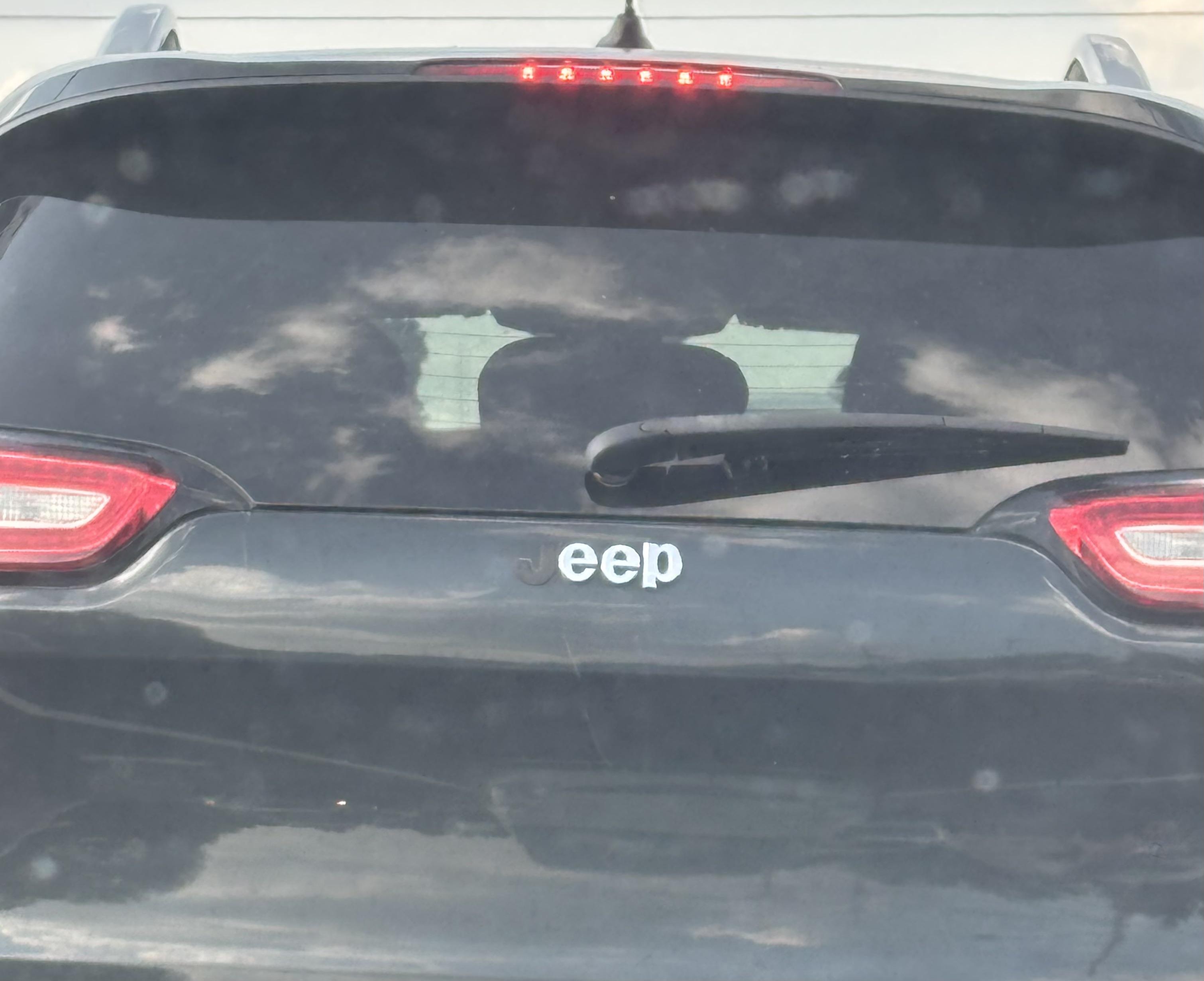 Car with missing J from Jeep logo, reads &quot;eep.&quot; Reflections of clouds and sky on rear windshield