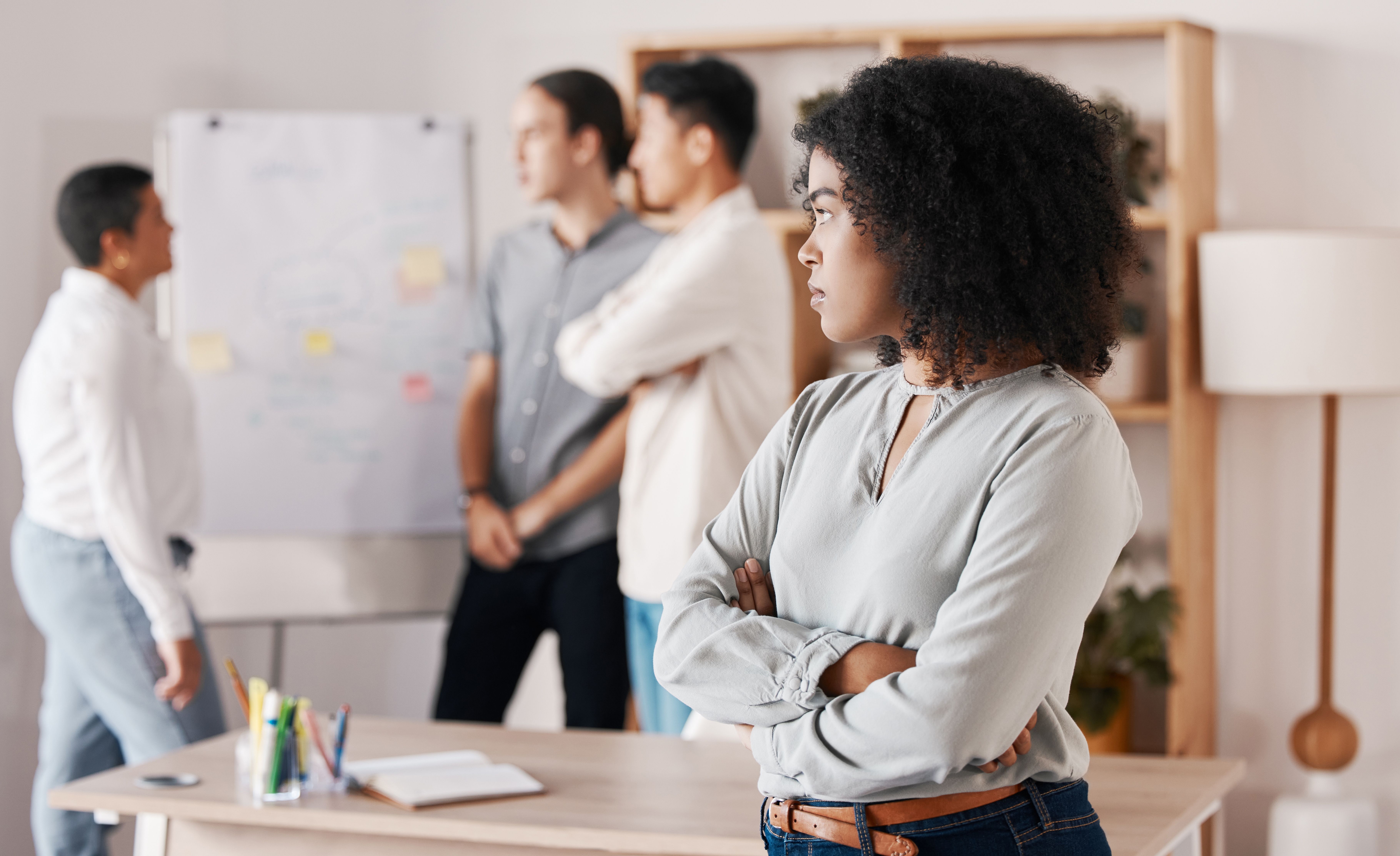 Person in professional attire looks at colleagues discussing by a whiteboard in an office setting