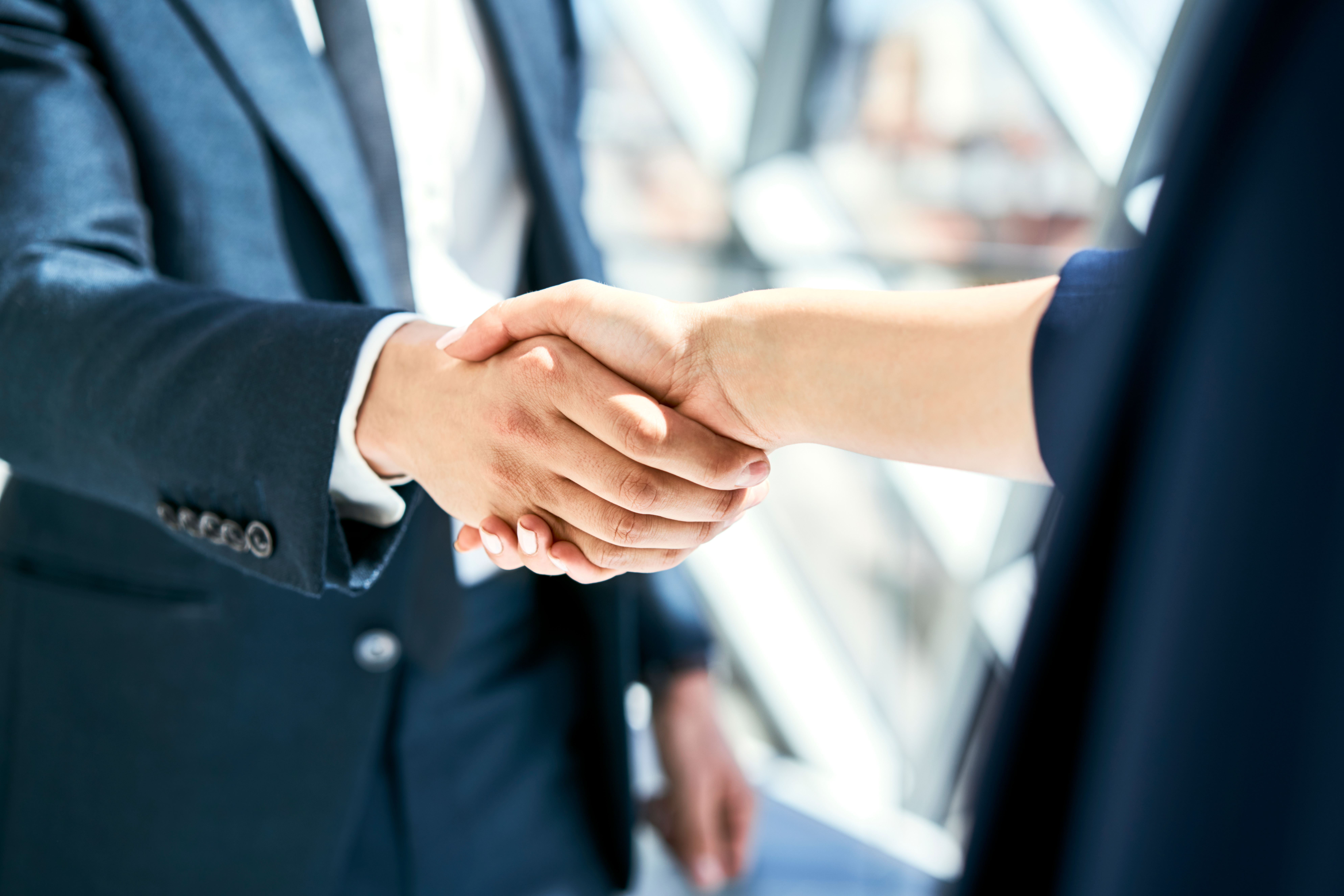 Two people in business attire shaking hands, signaling a professional agreement or collaboration in a work setting