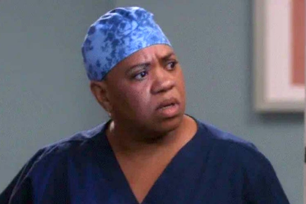 Person in medical scrubs and a patterned cap, looking surprised or concerned, in a hospital setting