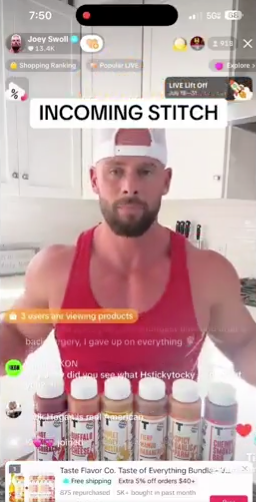 Man in sleeveless shirt stands behind a row of spice bottles during live broadcast, interacting with viewers&#x27; comments on-screen