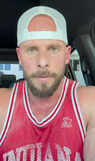 Man in a basketball jersey and white cap sitting in a car, looking at the camera