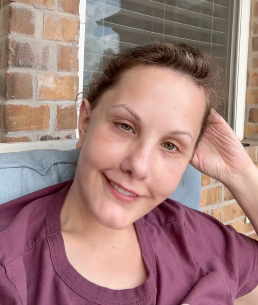 Person smiling while seated outdoors on a porch with a brick wall backdrop