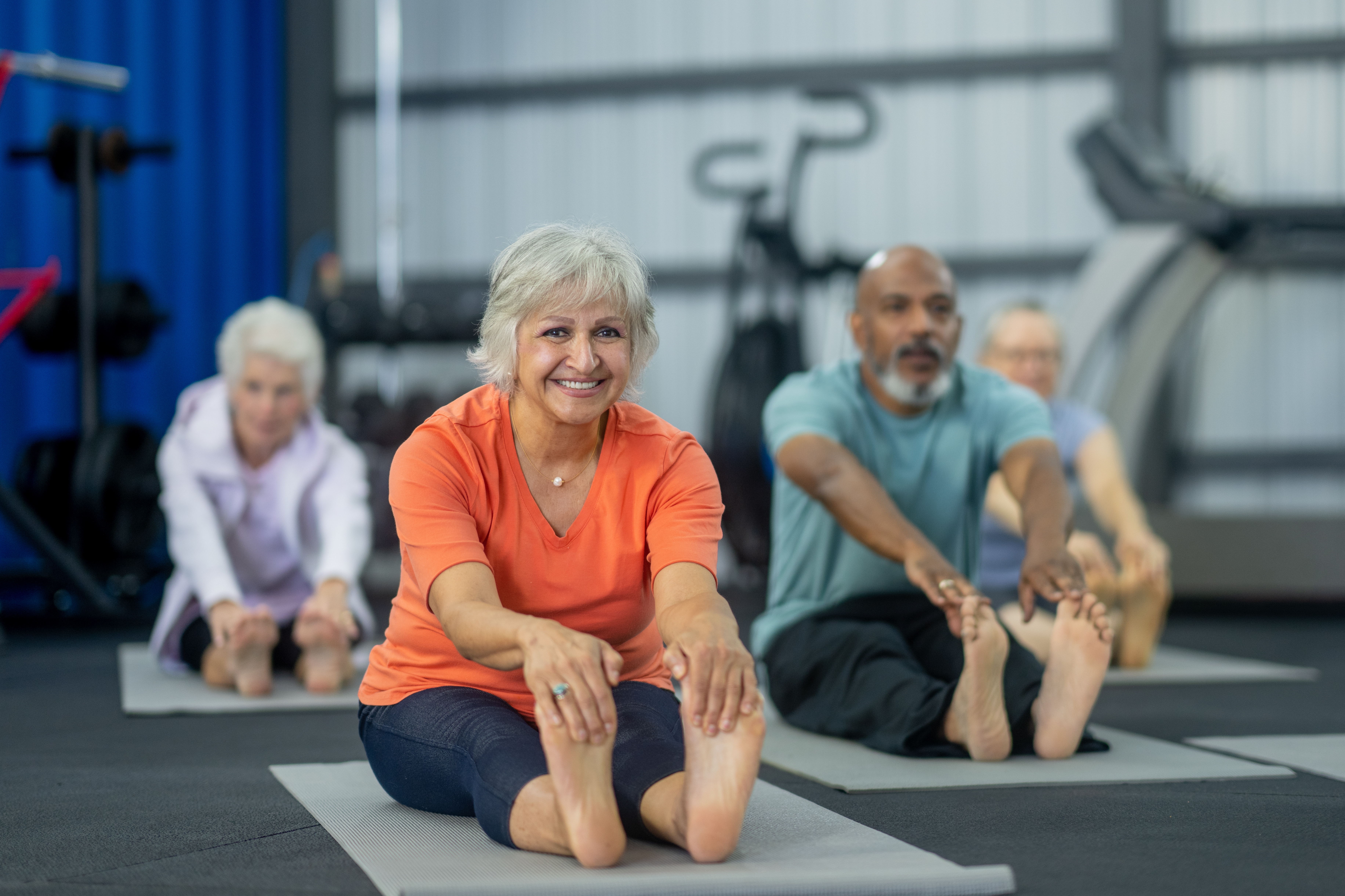 Older adults in a gym doing seated stretches on mats, smiling, promoting fitness and well-being