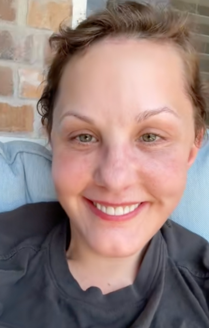 Person smiling while sitting on an outdoor couch, wearing a casual T-shirt