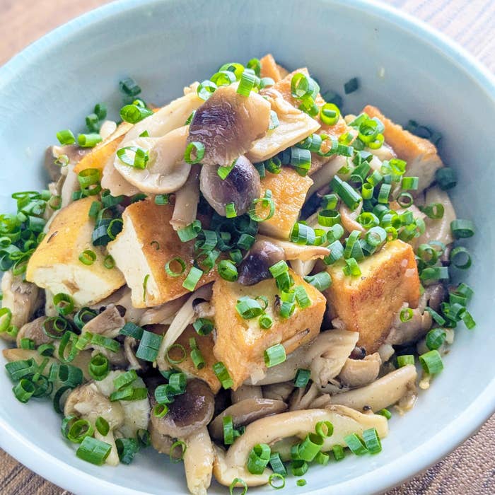キノコと豆腐の炒め物が白い器に盛られている。刻みネギが上にトッピングされている。