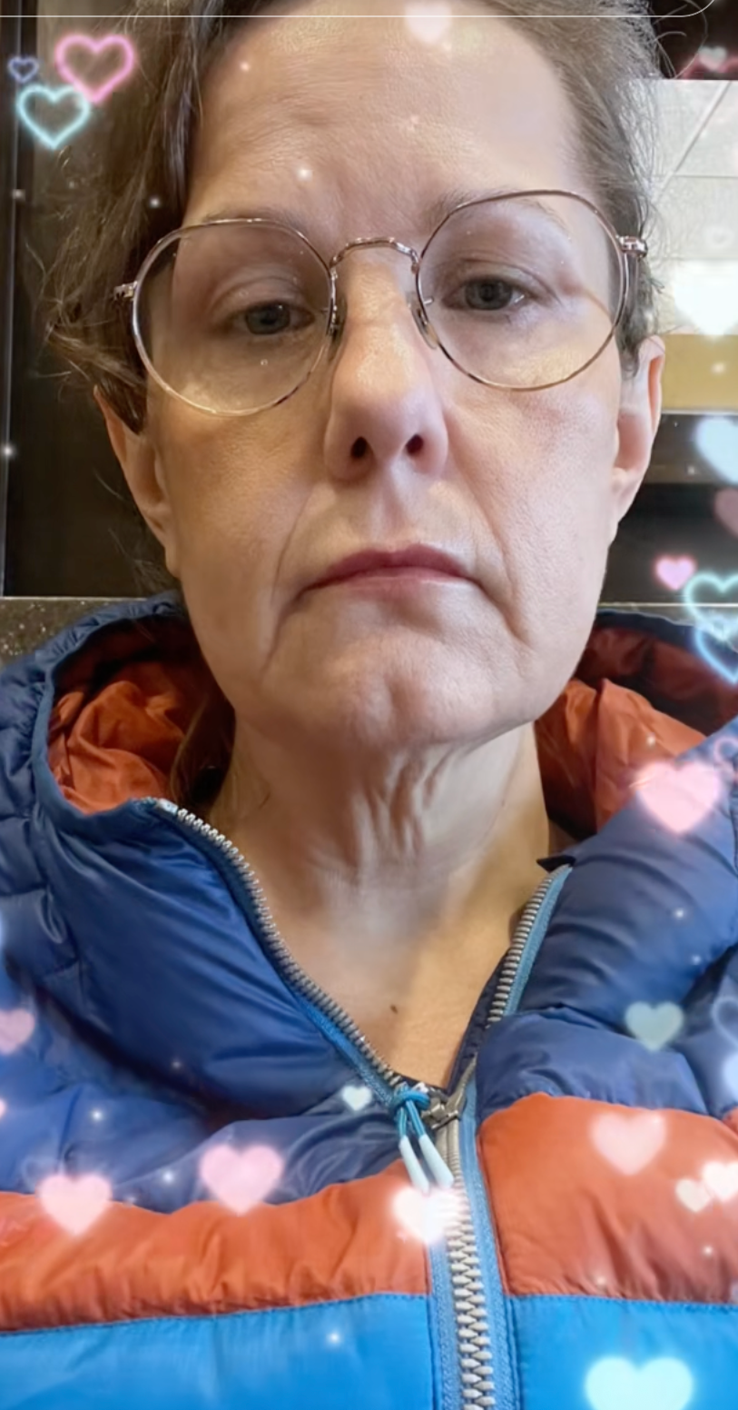 Person wearing glasses and a puffer jacket with a neutral expression, surrounded by heart effects
