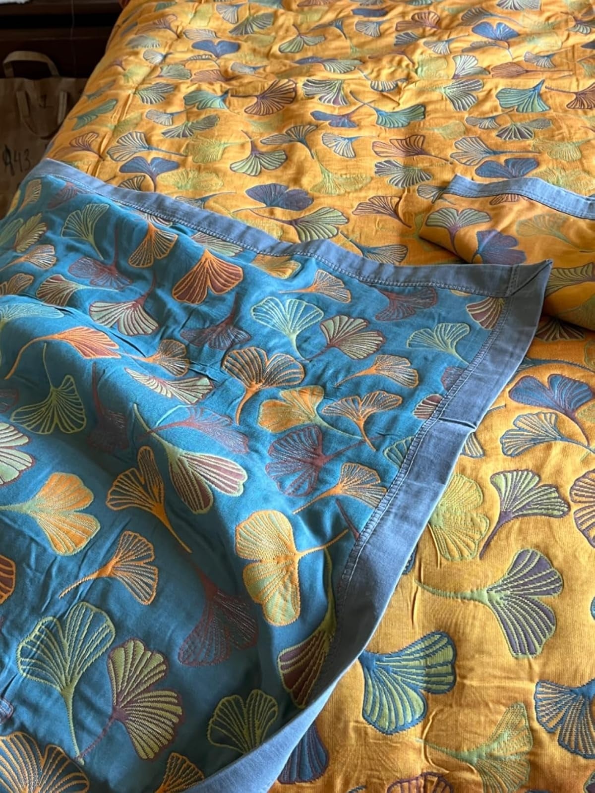 Close-up of a bedspread with a ginkgo leafage  signifier   connected  yellowish  and teal fabric, showcasing the bedding's elegant plan  and texture
