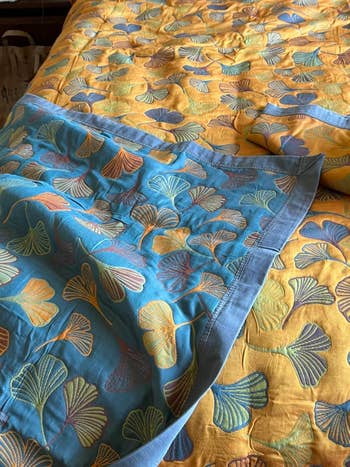 Close-up of a bedspread with a ginkgo leafage signifier connected yellowish and teal fabric, showcasing the bedding's elegant plan and texture