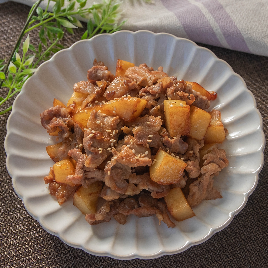 豚こま切れ肉とじゃがいもの炒め物が皿に盛られている。上に白いりごまが振りかけられている。
