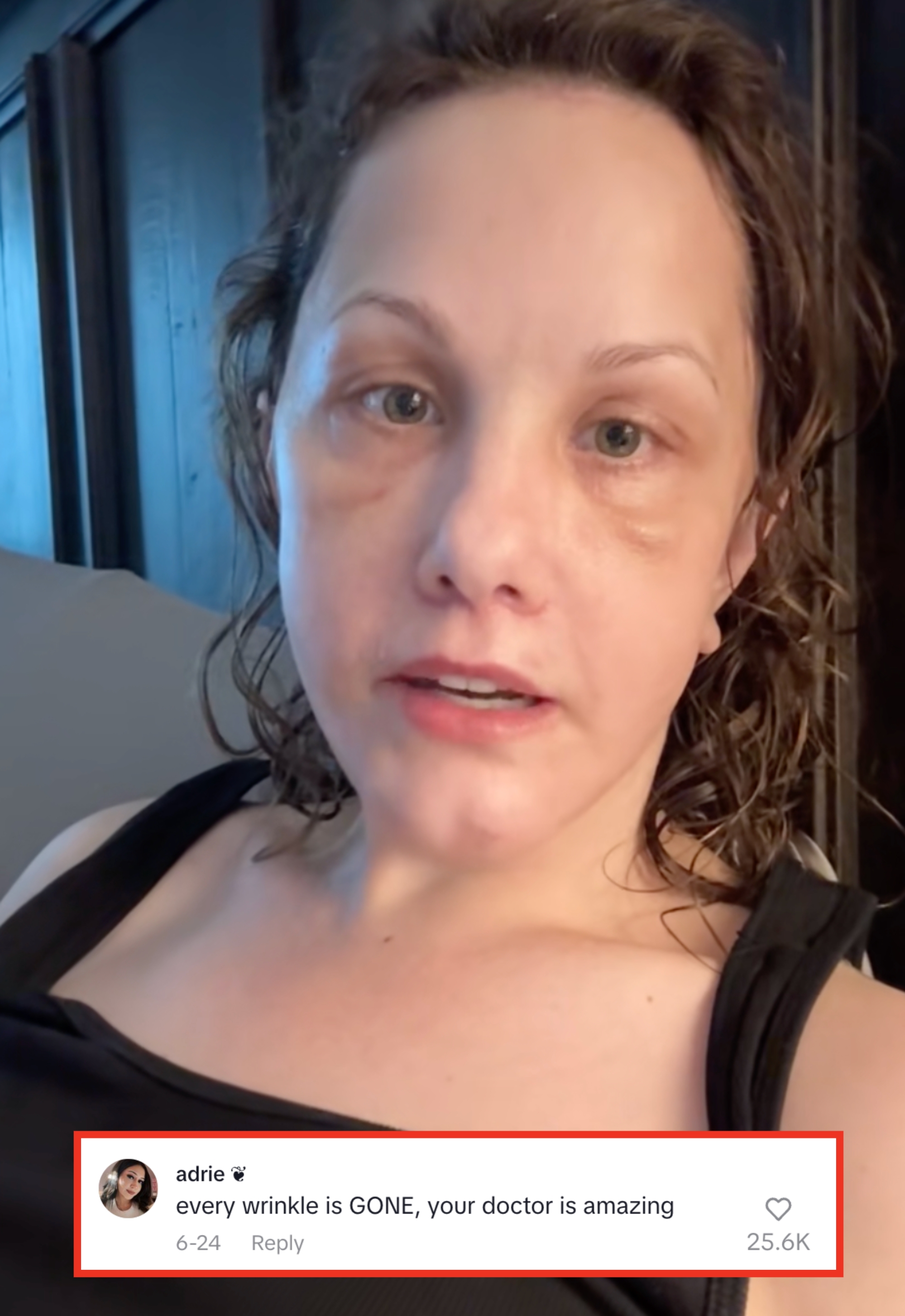 Person with wet hair in a casual black top, relaxed at home, appearing to talk or engage with the camera. Background features wooden paneling