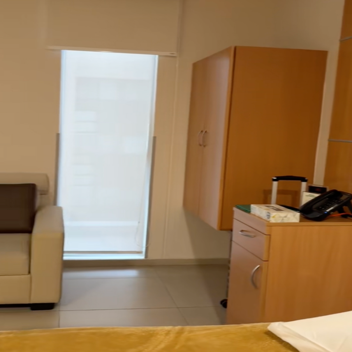 Modern waiting room with a sofa, cabinet, and a phone on a countertop. Bright natural light from a tall window