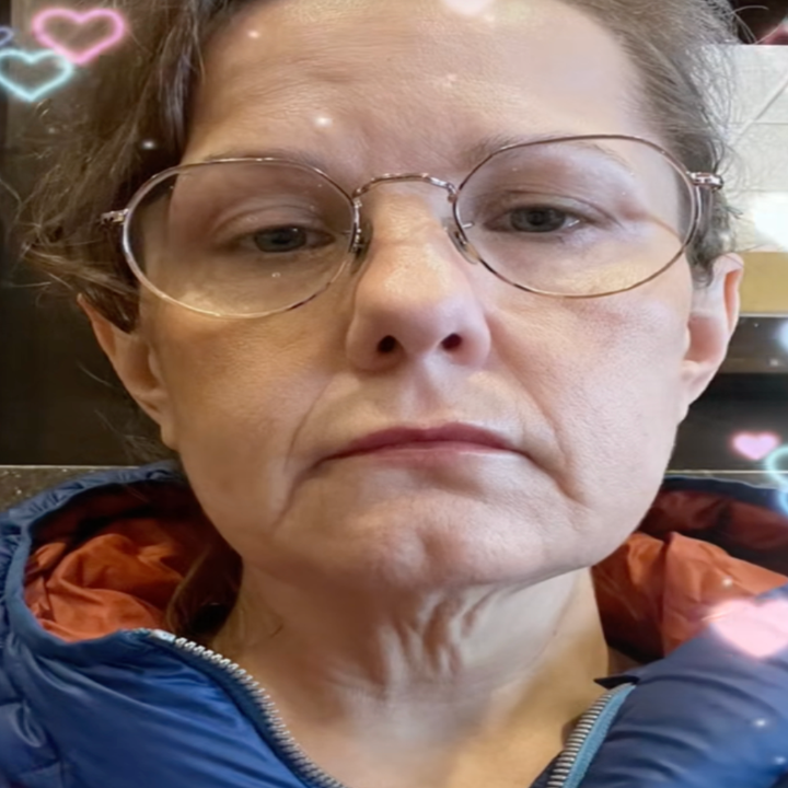 Person with neutral expression, wearing large round glasses and a jacket with a visible inner lining. Hearts are digitally overlaid around them
