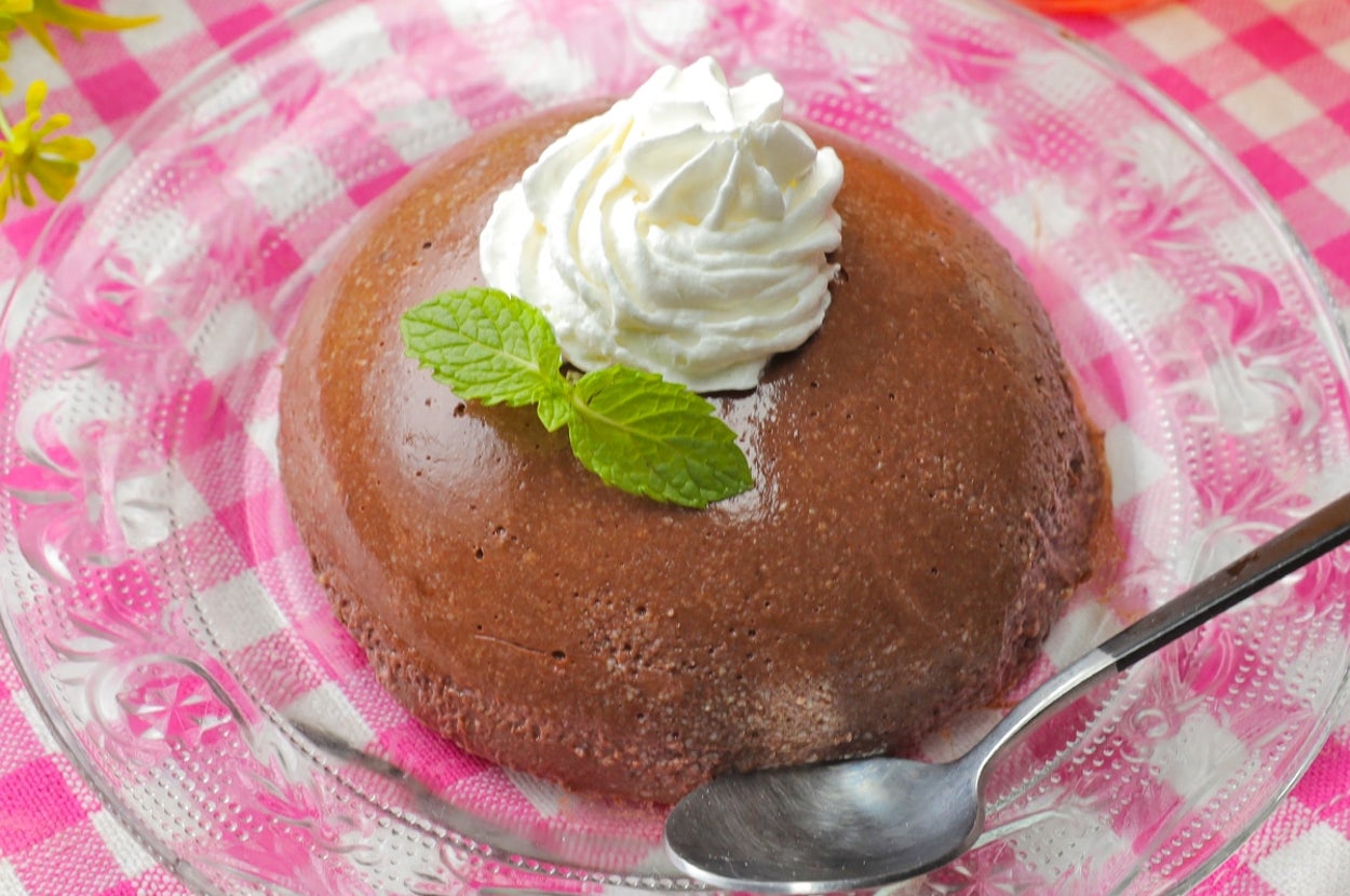 デザート皿に盛られたチョコレートプリンにホイップクリームとミントがのっている。横にスプーンが添えられている。