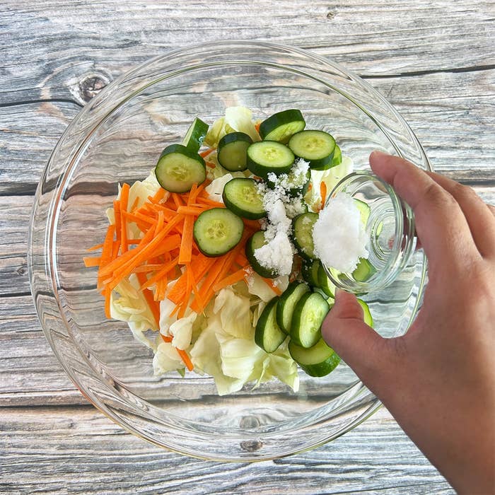 ガラスボウルに入った野菜に塩を加えている。