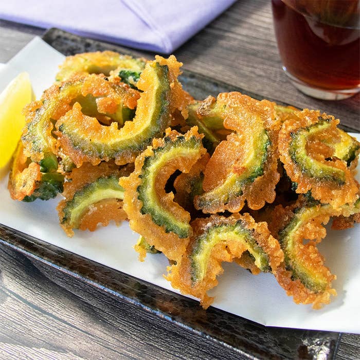 唐揚げの粉を使って作ったゴーヤの唐揚げが皿に盛られている。レモンが添えられ、飲み物が横に置かれている。