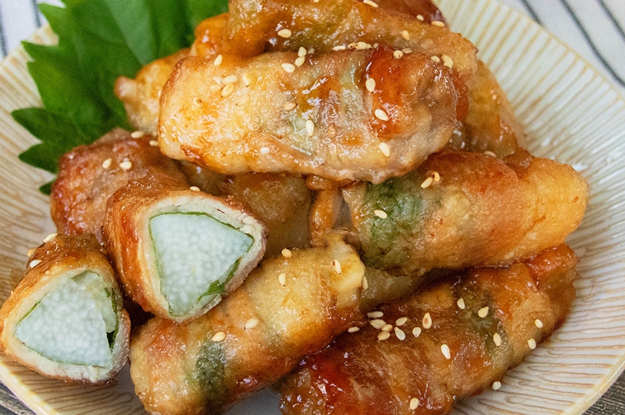 白い皿に盛られた長芋と大葉の肉巻き、白いりごまが散らしてある。
