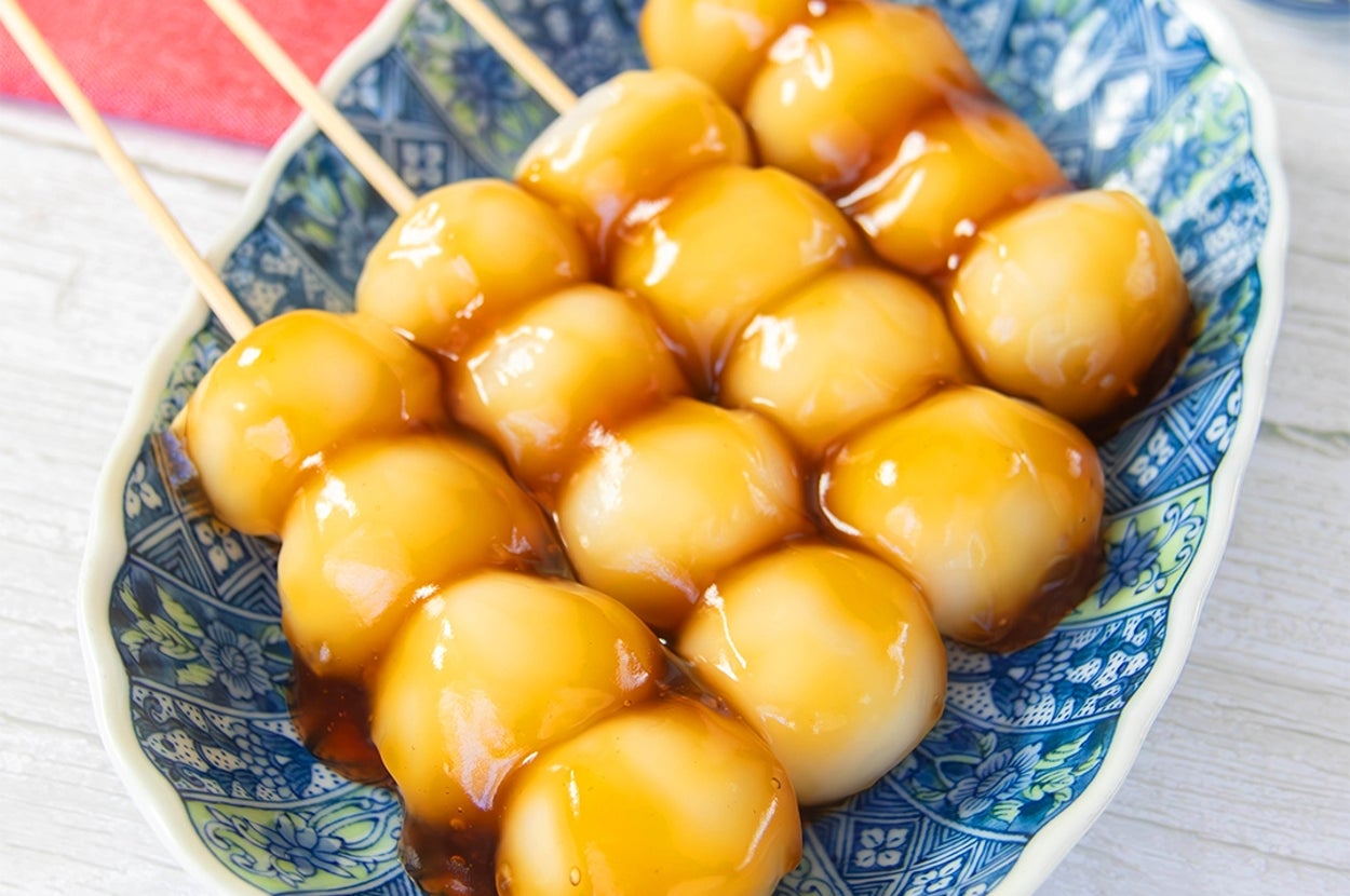 皿に並んだ白玉粉で作ったみたらし団子の串。甘辛だれがかかっている。