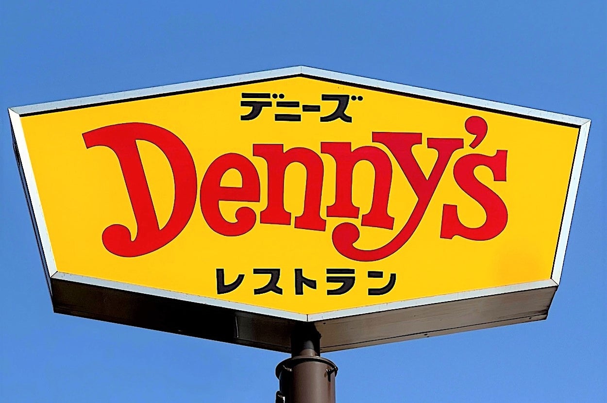 Denny's restaurant sign featuring Japanese text under the logo, mounted on a pole with a clear sky background