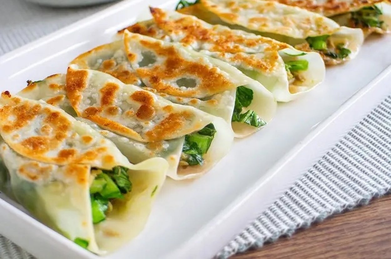 白い皿に整然と並ぶ焼き餃子と醤油の入った小皿。背景にガラスの飲み物。
