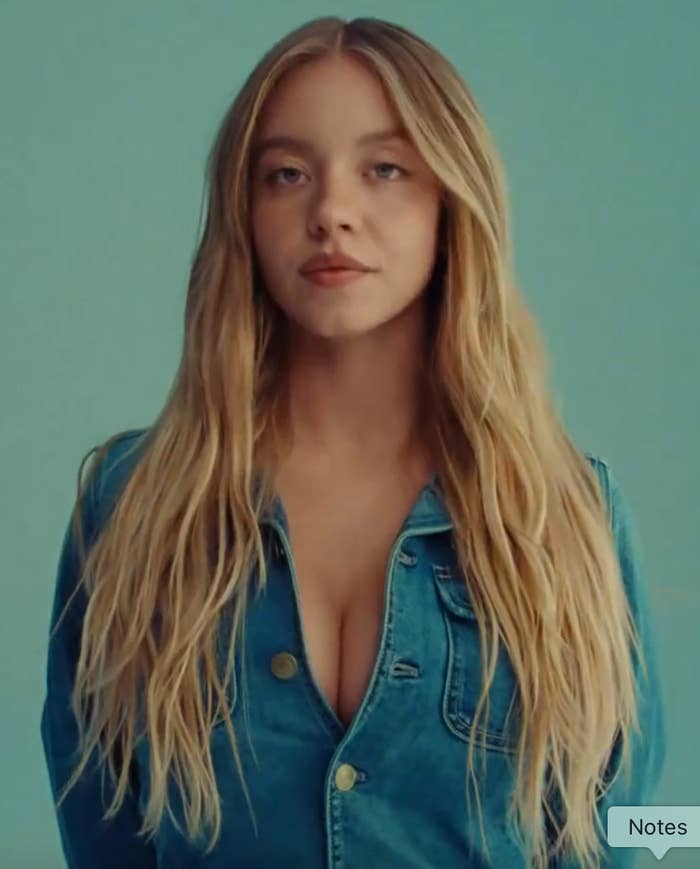 Person with long hair wearing a denim top with buttons undone, looking forward