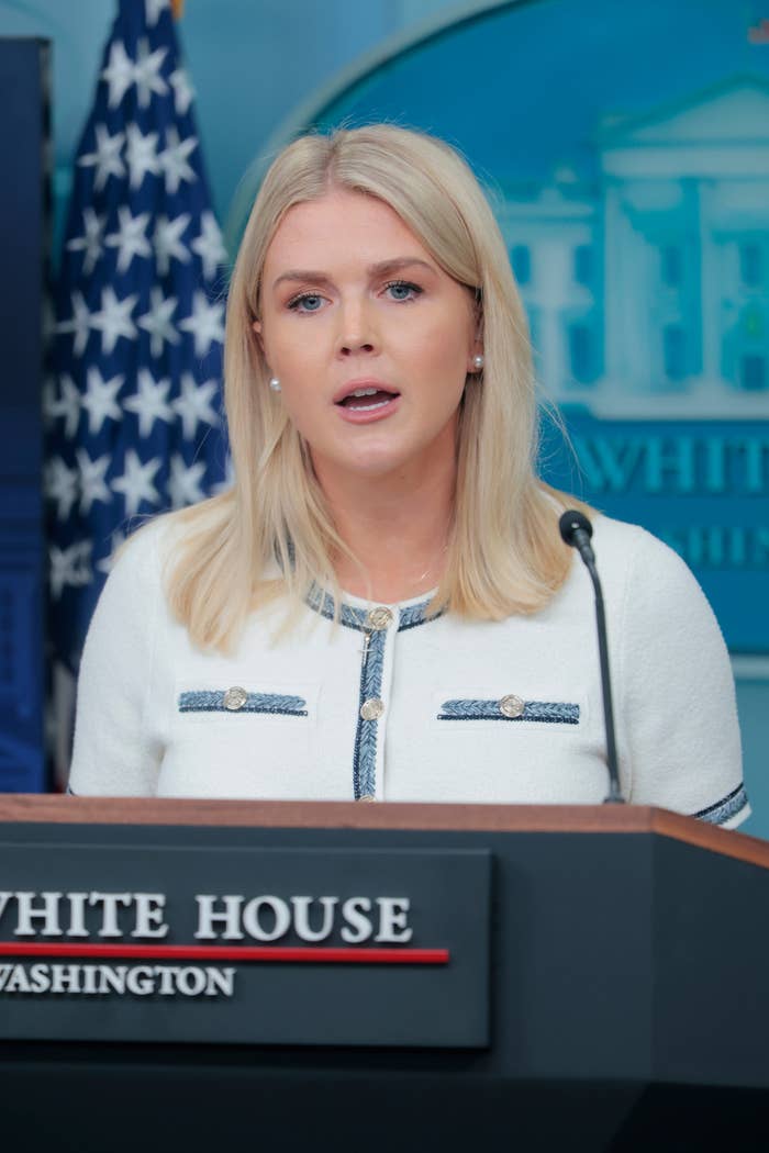 Person speaking at a podium with a White House logo, in front of a U.S. flag, wearing a professional blazer