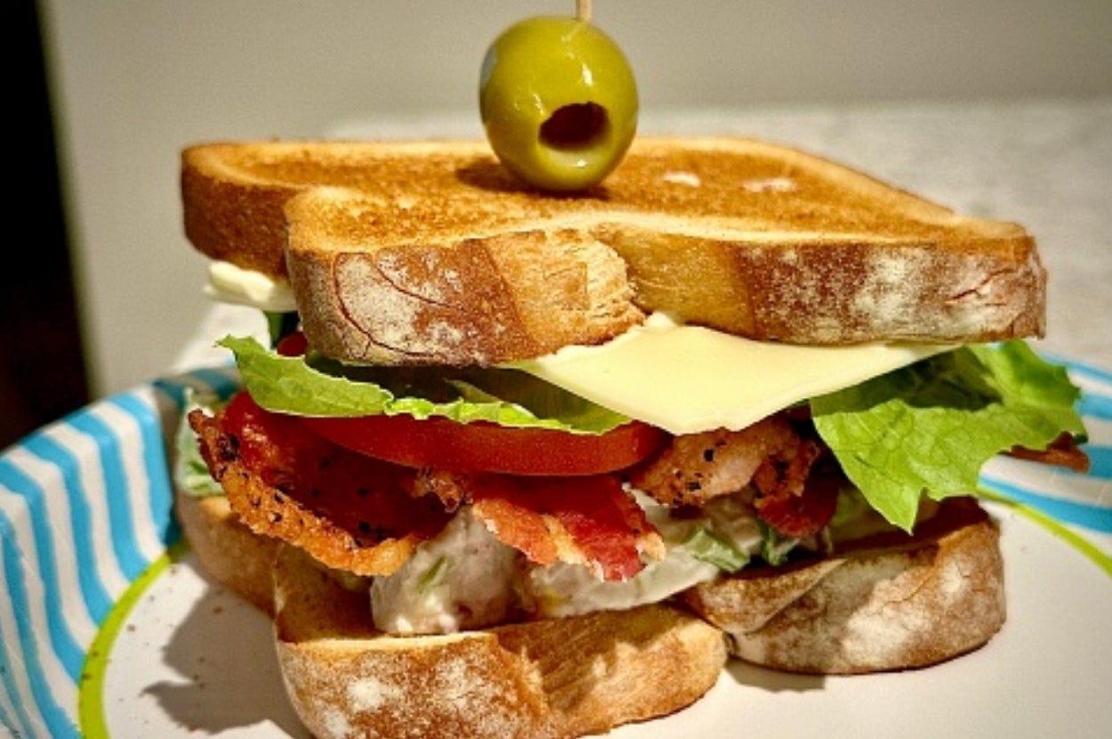 A classic BLT sandwich with crispy bacon, lettuce, tomato, cheese, and mayonnaise on toasted bread, topped with an olive on a toothpick